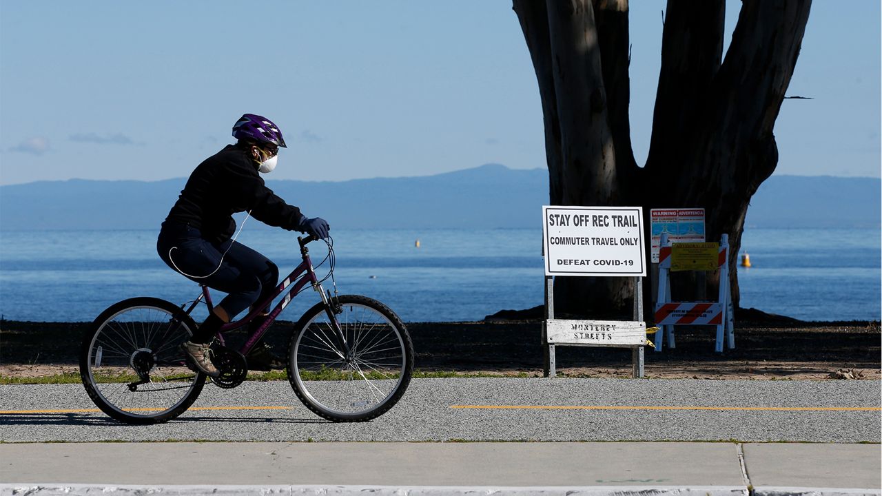 In this photo taken Tuesday April 7, 2020 a sign calling for the defeat of COVID-19 warns people the Monterey Bay Coastal Trail , in Monterey, Calif. is for commuter travel only,. The scenic Monterey Peninsula, that derives much of its economy from tourism, has been hit hard with the closing of many major attractions and restaurants. (AP Photo/Rich Pedroncelli)