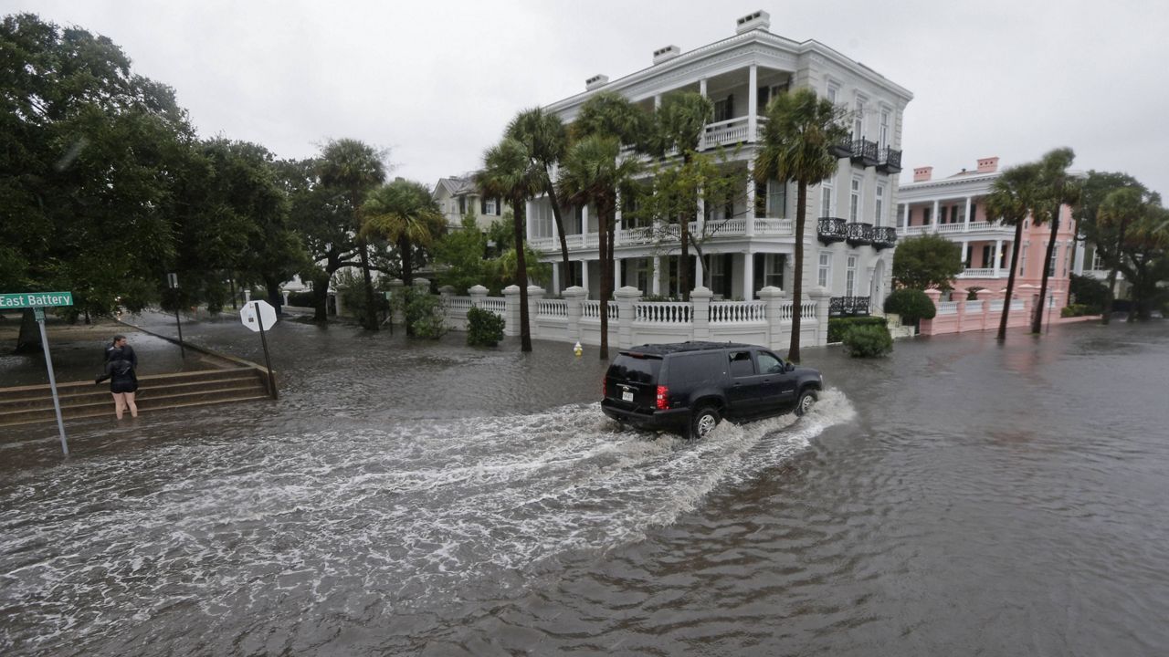 In this Oct. 3, 2015, file photo, a driver takes his truck through a flooded street in Charleston, S.C. (AP Photo/Chuck Burton, File)