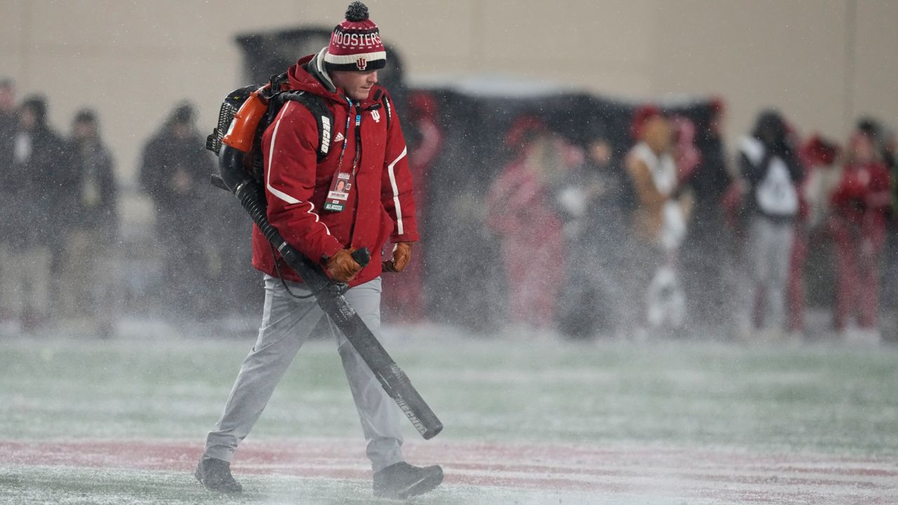 A worker cleans snow from the field during the first half of an NCAA college football game between Indiana and Purdue, Nov. 30, 2024, in Bloomington, Ind. 