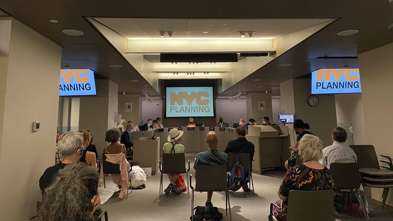 Socially-distant members of the public sit in chairs facing the City Planning Commission's board members with three screens above with text "NYC PLANNING."