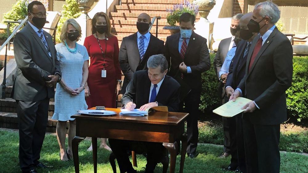 North Carolina Gov. Roy Cooper, center, signs police reform bills into law while legislators and others watch during a ceremony outside the Executive Mansion in Raleigh, N.C., Thursday, Sept. 2, 2021 (AP Photo/Gary D. Robertson).