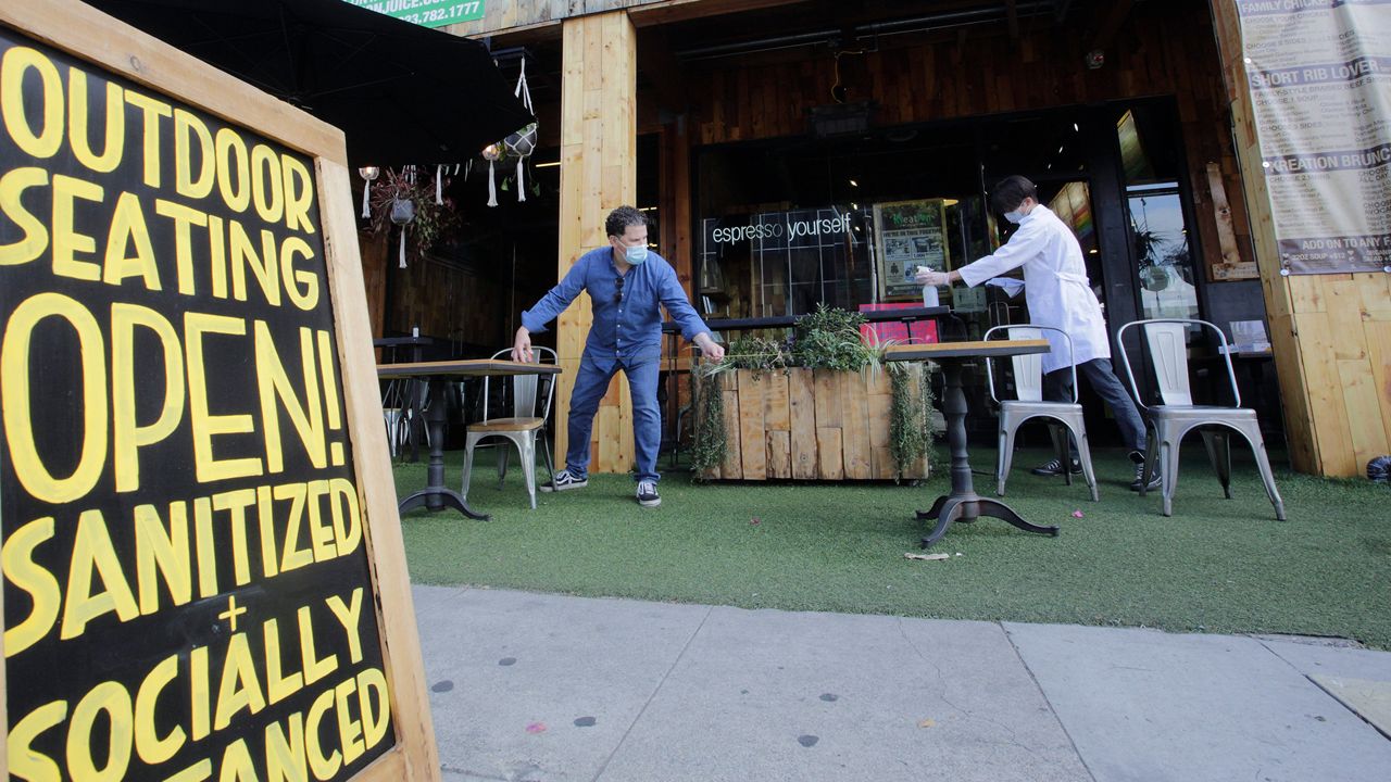 Kreation Organic manager Frank D'Andrea, left, measures a required six-feet distance between tables as his staff gets ready for customers to sit outdoors in Los Angeles, Friday, May 29, 2020. Populous Los Angeles County won approval Friday to reopen restaurants and hair-cutting businesses to customers. At the same time, remote Lassen County, the first California jurisdiction to backpedal on a reopening plan, reversed itself again and decided to allow in-person dining and shopping in stores after determining it mitigated its first small outbreak of coronavirus cases. (AP Photo/Damian Dovarganes)