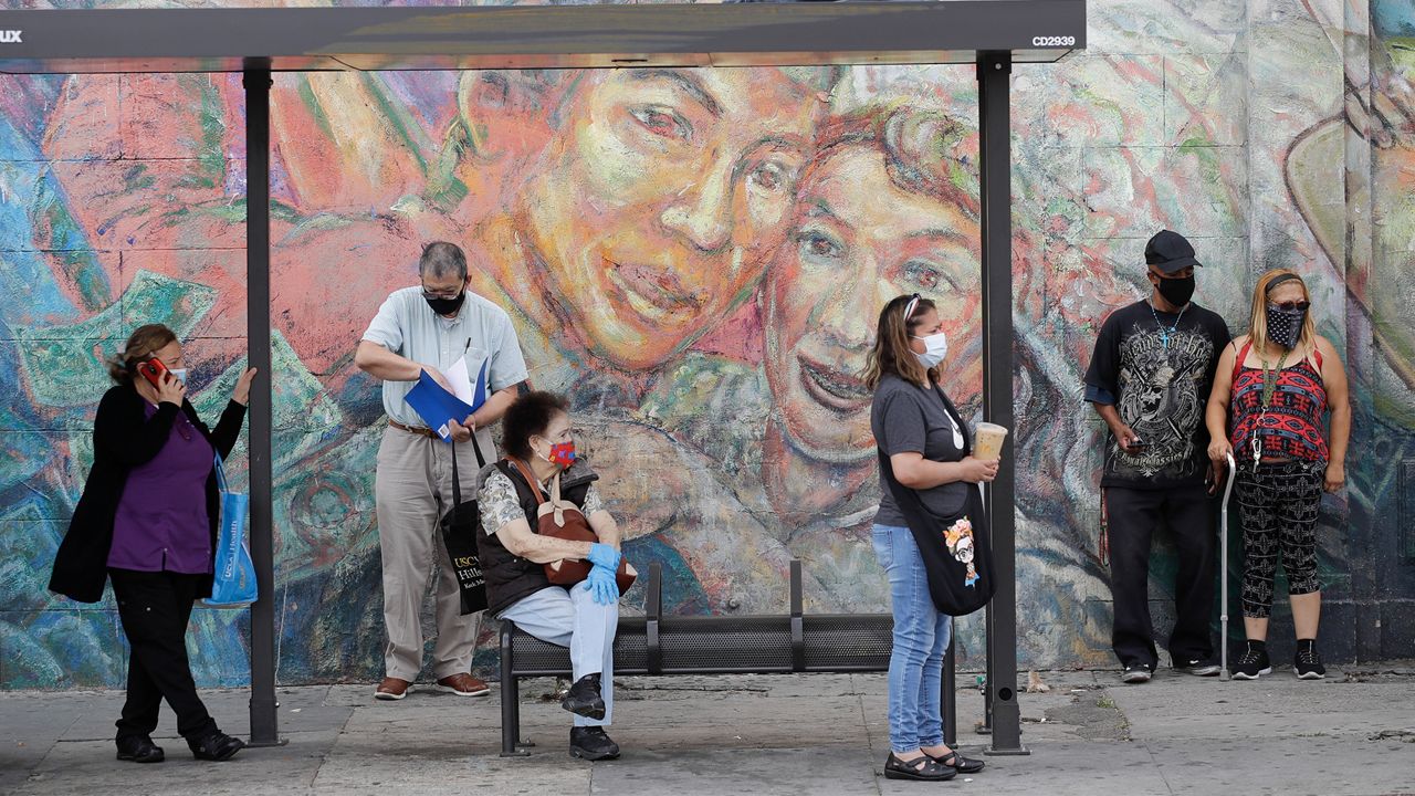 People wear masks as they wait at a bus stop amid the coronavirus pandemic Monday, June 29, 2020, in Los Angeles. (AP Photo/Marcio Jose Sanchez)