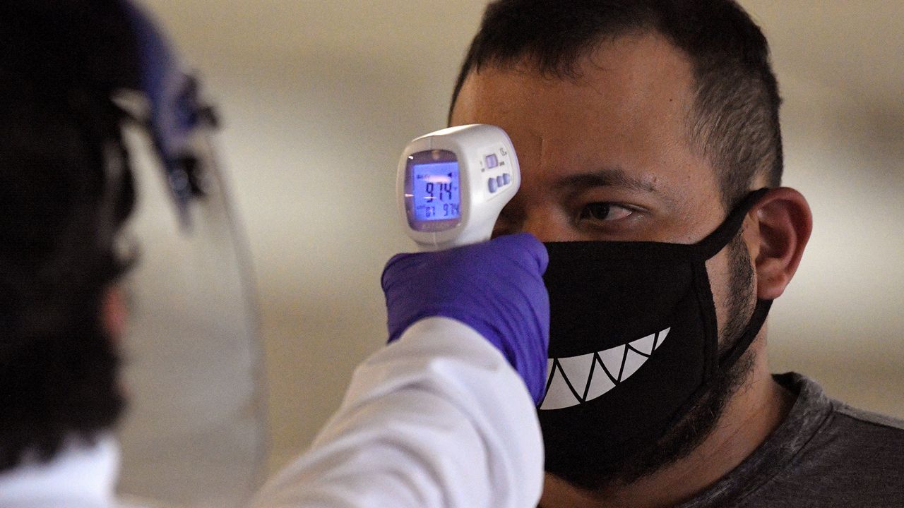 Jose Ramirez has his temperature checked before entering Universal CityWalk, Thursday, June 11, 2020, near Universal City, Calif. The tourist attraction, which had been closed due to the coronavirus outbreak recently re-opened. The Universal Studios tour is still closed. (AP Photo/Mark J. Terrill)