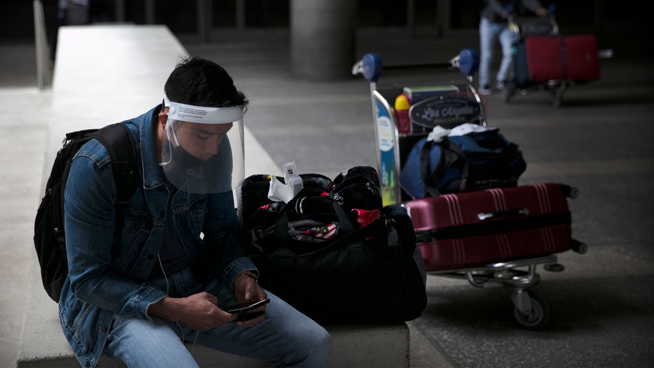 A traveler wearing a face shield looks at his phone outside the arrivals area at Los Angeles International Airport on Wednesday, June 24, 2020, in Los Angeles. The United States recorded a one-day total of 34,700 new COVID-19 cases, the highest in two months, according to the count kept by Johns Hopkins University. (AP Photo/Jae C. Hong)