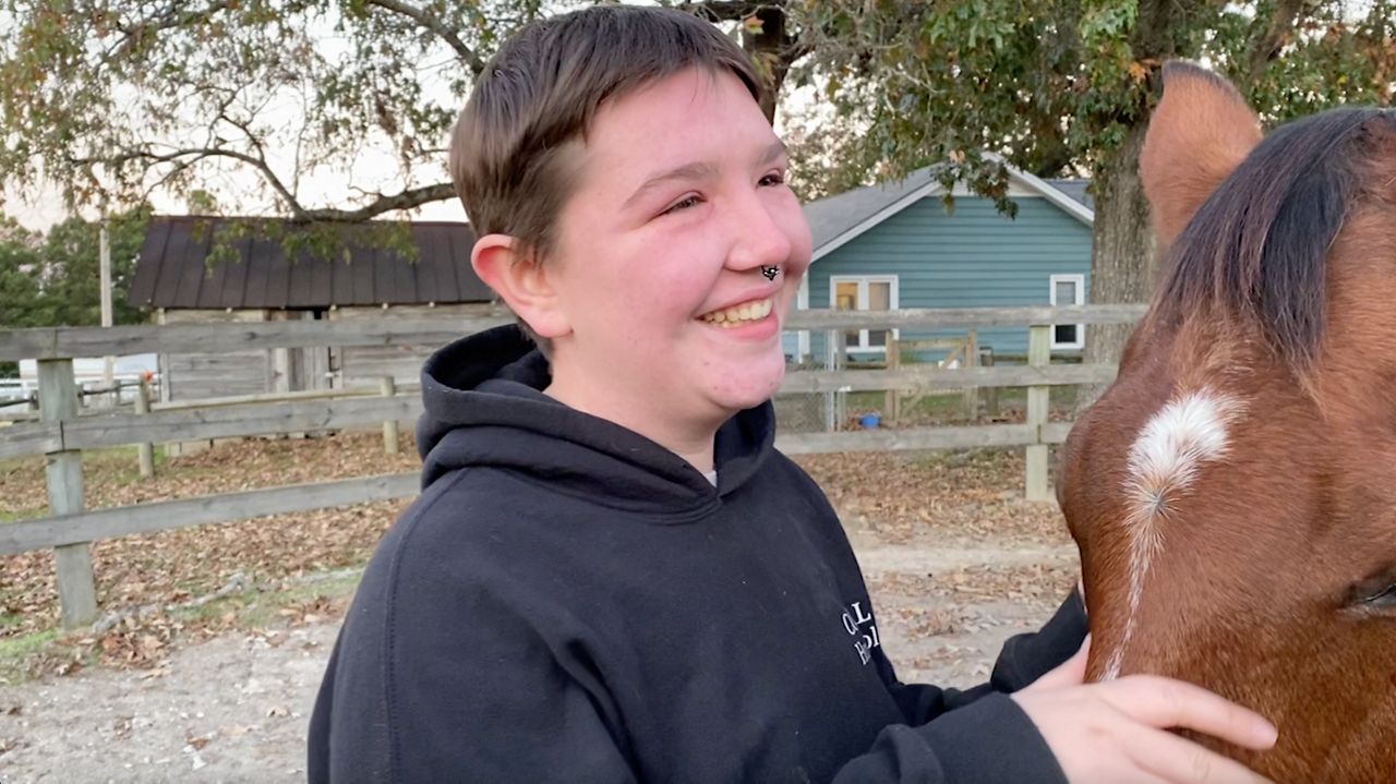 DJ Sinodis, a riding academy participant at CORRAL, smiles next to her horse River.