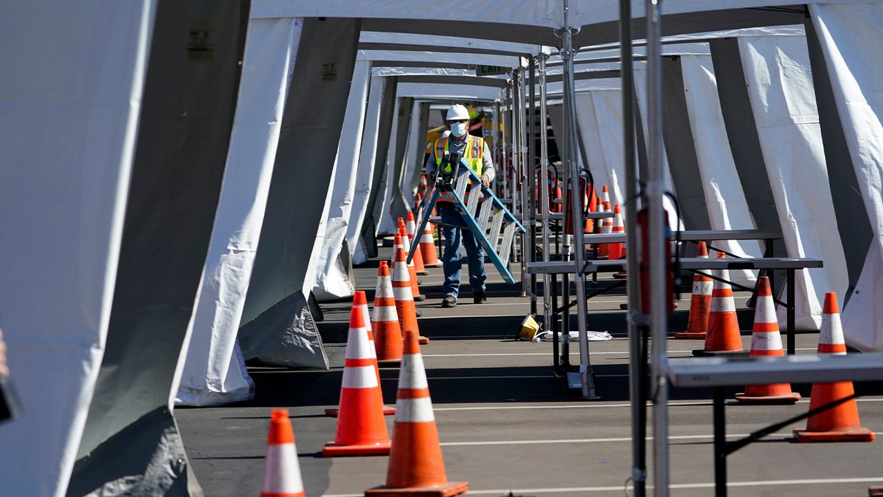 A worker carries a ladder as he prepares tents at a new federal COVID-19 vaccination center on the campus of the California State University Los Angeles Friday, Feb. 12, 2021, in Los Angeles. (AP Photo/Marcio Jose Sanchez)