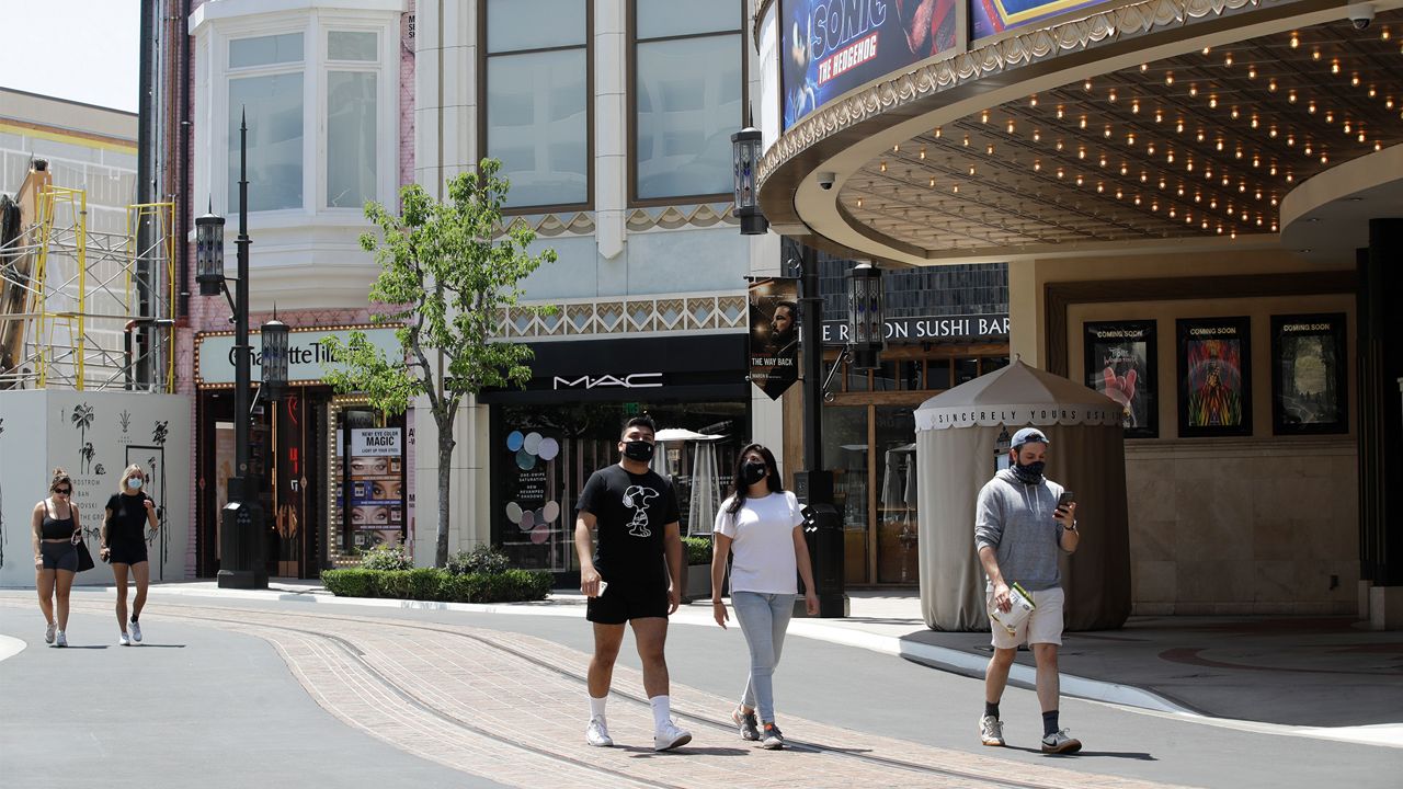 People walk in a mostly empty The Grove shopping center Wednesday, May 27, 2020, in Los Angeles. California moved to further relax its coronavirus restrictions and help the battered economy. Retail stores, including those at shopping malls, can open at 50% capacity. (AP Photo/Marcio Jose Sanchez)