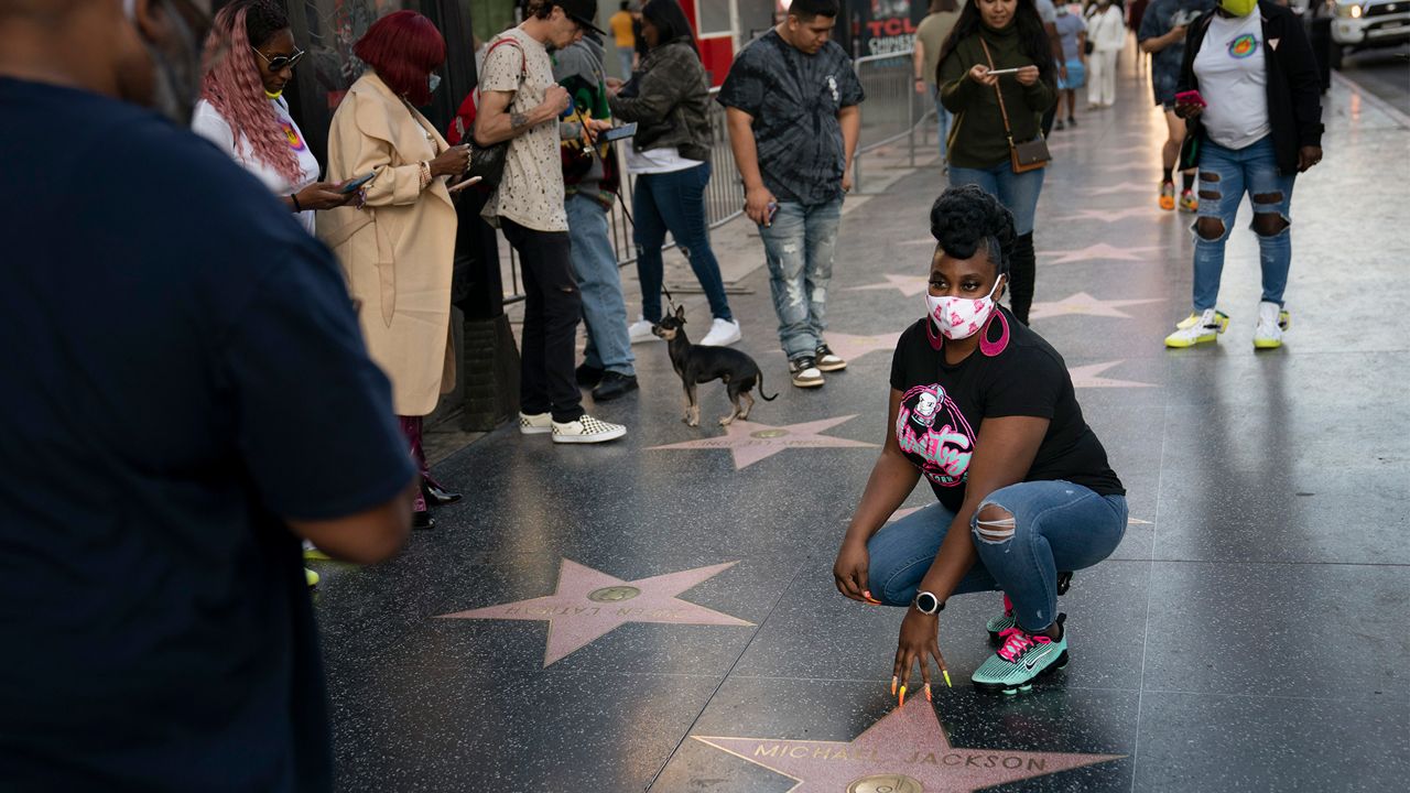 A tourist in a face mask pauses for photos with Michael Jackson's star on the Hollywood Walk of Fame in Los Angeles, Thursday, Nov. 12, 2020. (AP Photo/Jae C. Hong)