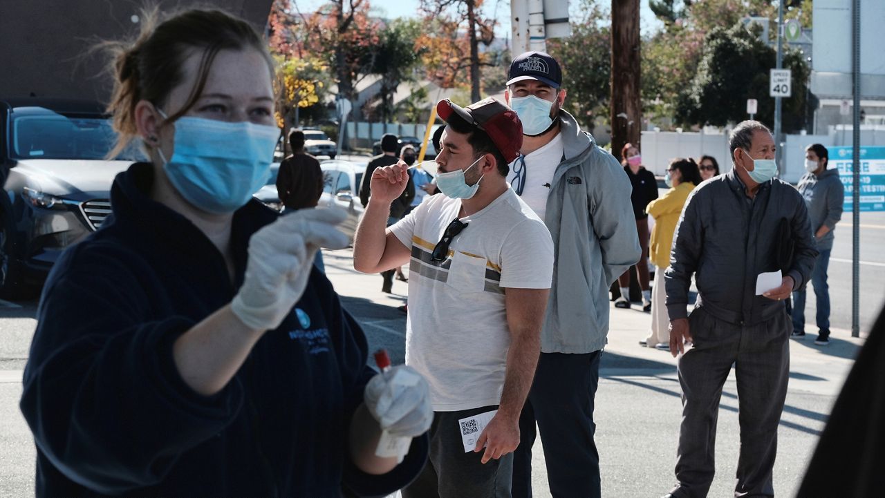 A man is handed a swab for a Covid-19 rapid test as people line up at a gas station in the Reseda section of Los Angeles on Sunday, Dec. 26, 2021. (AP Photo/Richard Vogel)
