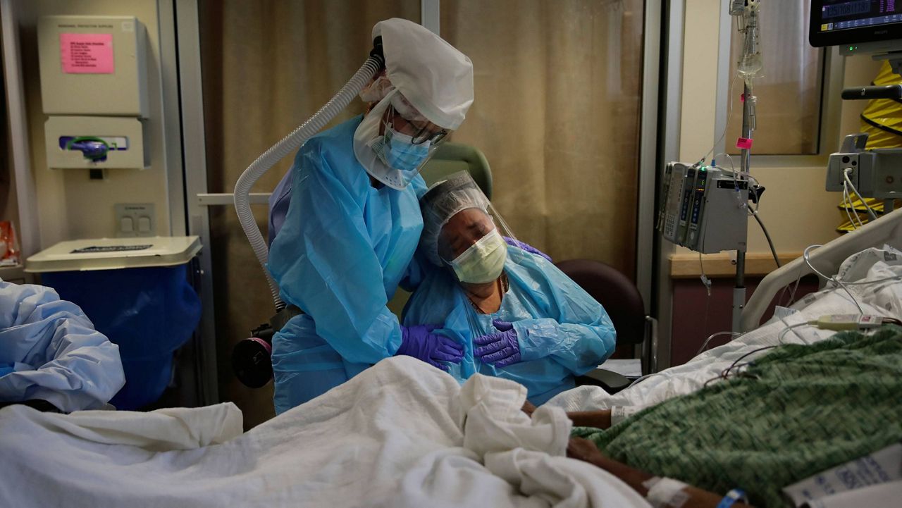 Romelia Navarro, right, is comforted by nurse Michele Younkin as she weeps while sitting at the bedside of her dying husband, Antonio, in St. Jude Medical Center's COVID-19 unit in Fullerton, Calif., on July 31, 2020. (AP Photo/Jae C. Hong, File)