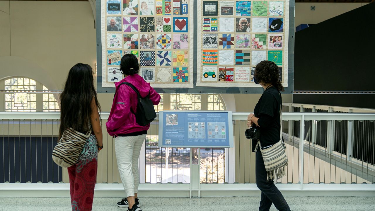 High school students pause in front of a few panels of Madeleine Fugate's COVID Memorial Quilt to honor those who died of COVID-19, displayed at the California Science Center in Los Angeles on Tuesday, Oct. 19, 2021. (AP Photo/Damian Dovarganes)