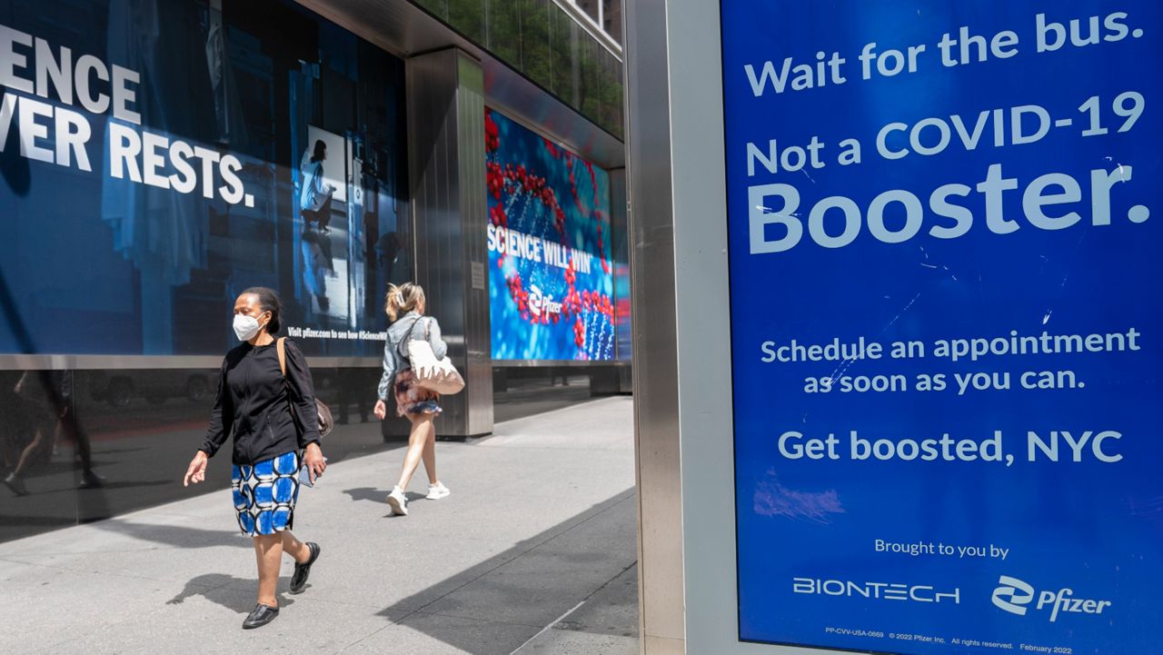 A pedestrian walks down the sidewalk in New York City next to a bus station advertising COVID-19 booster doses.