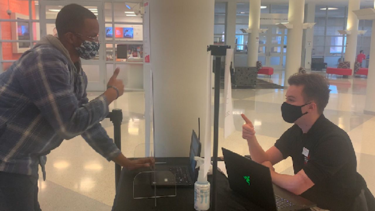 College students gives the thumbs up sign to an another person in front of a computer.
