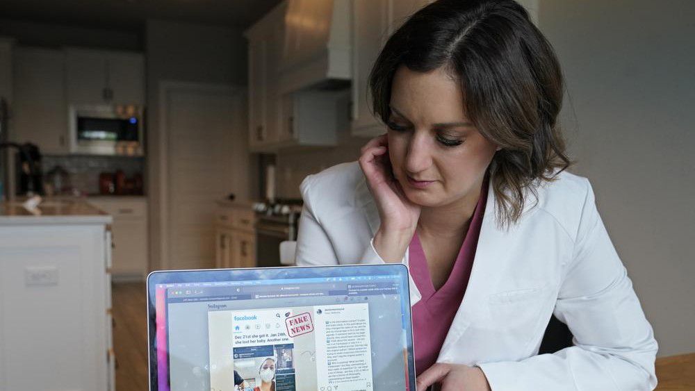 Dr. Michelle Rockwell, who was targeted by vaccine opponents after she posted about her miscarriage online, looks at her Instagram page with her hijacked post marked as fake news during an interview at her home Wednesday, April 28, 2021, in Jenks, Okla.  (AP Photo/Sue Ogrocki)