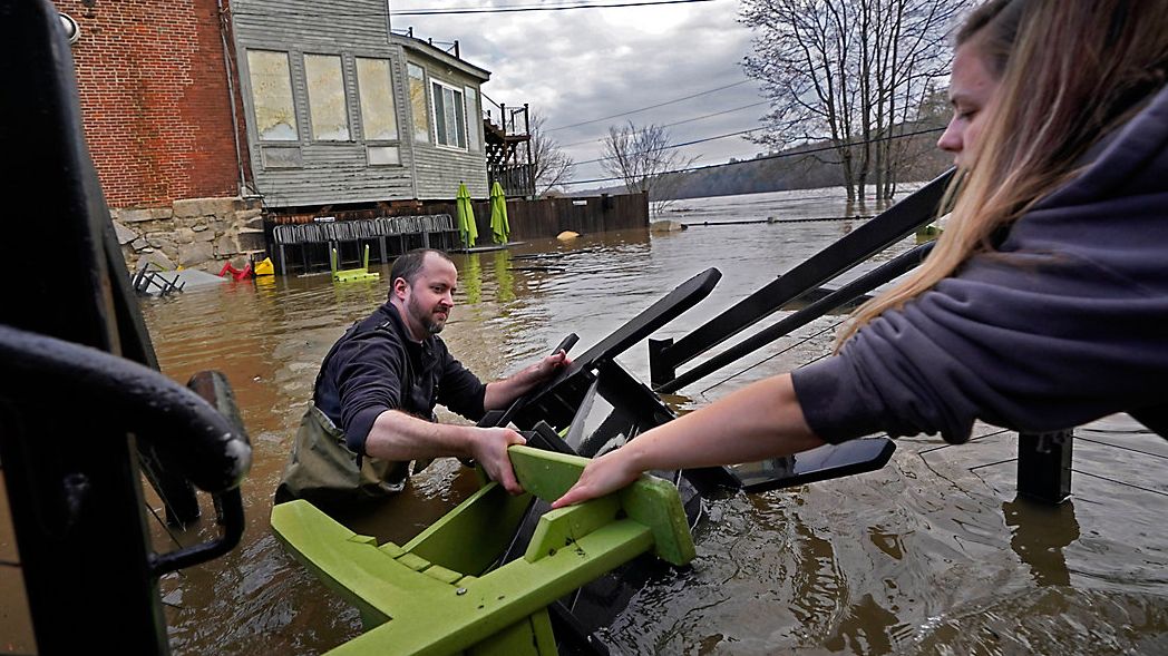 Nathan Sennett hands furniture to Tori Grasse as they work in hip-deep water on the patio of the Quarry Tap Room, Tuesday, Dec. 19, 2023, in Hallowell, Maine. Waters continue to rise in the Kennebec River following Monday's severe storm. (AP Photo/Robert F. Bukaty)