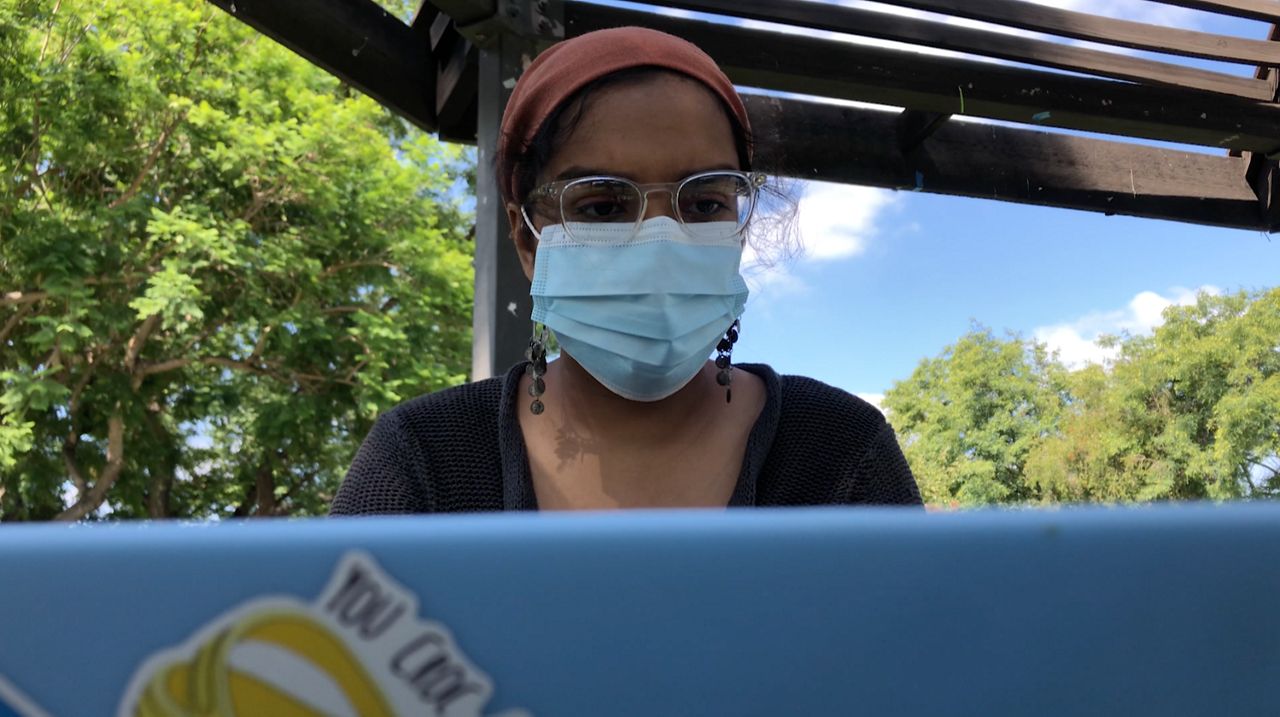 A student wearing a mask sitting at a laptop