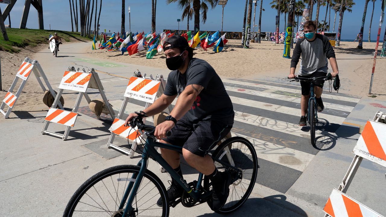 Cyclists wearing masks to protect from coronavirus cross a closed section of Venice beach on Friday, July 3, 2020 in Los Angeles. California's governor is urging people to wear masks and skip Fourth of July family gatherings as the state's coronavirus tally rises. All L.A. County beaches are closed from July 3 through July 6, to prevent dangerous crowding. Rates of COVID-19 infections and hospitalizations have soared in the past two weeks after falling last month. (AP Photo/Richard Vogel)