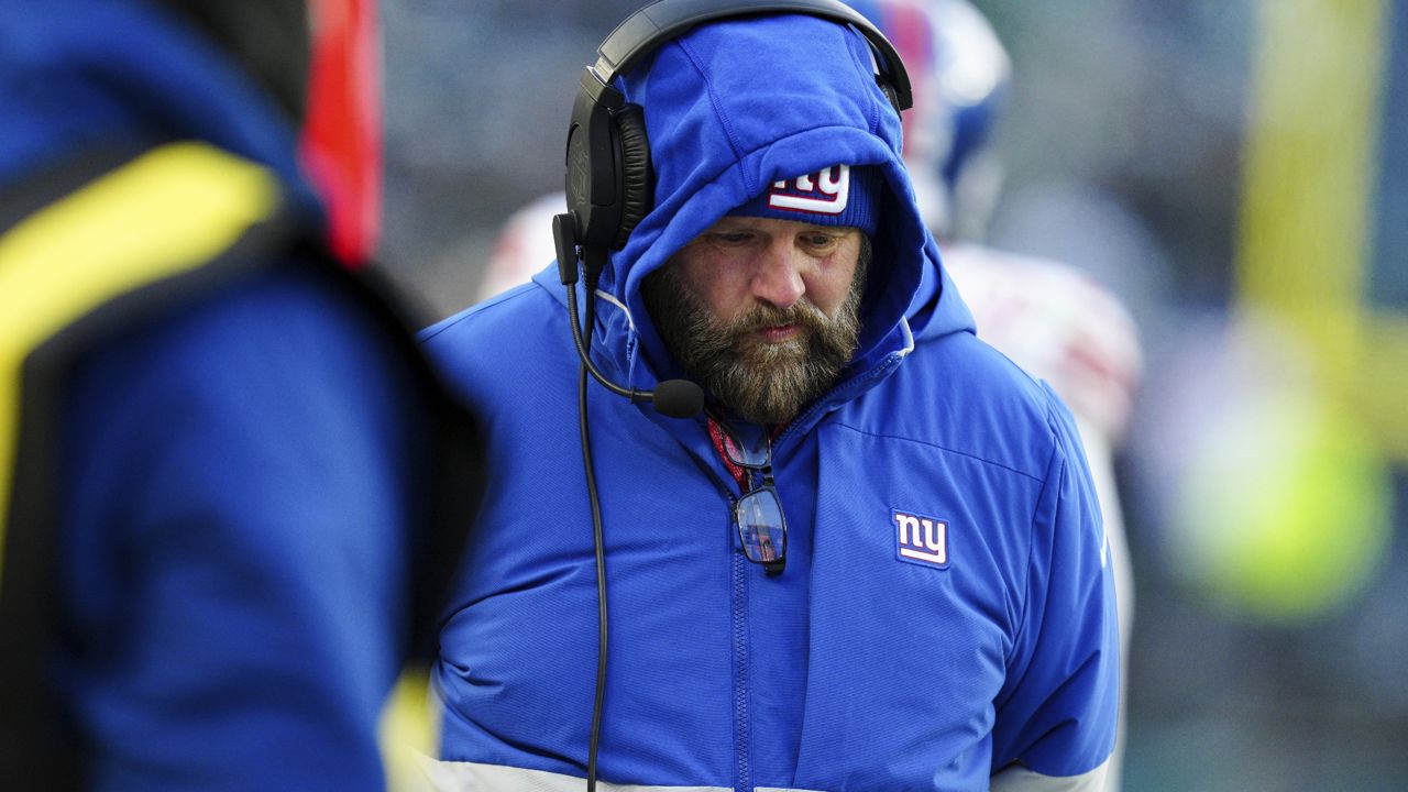 brian daboll, in blue new york giants hat and coat, looks downward on sideline