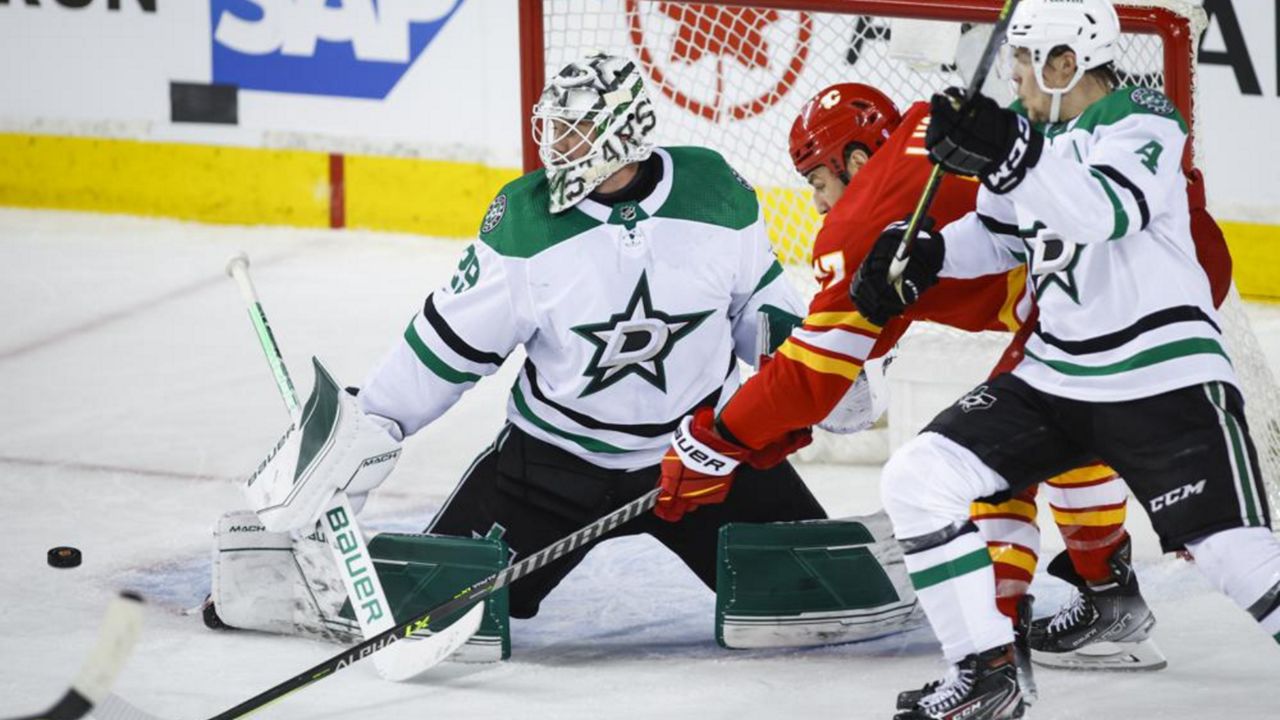 Dallas Stars goalie Jake Oettinger, left, kicks the puck away from Calgary Flames left wing Milan Lucic, center, as Flames' Miro Heiskanen defends during the second period of Game 2 of an NHL hockey Stanley Cup first-round playoff series in Calgary, Alberta, Thursday, May 5, 2022. (Jeff McIntosh/The Canadian Press via AP)