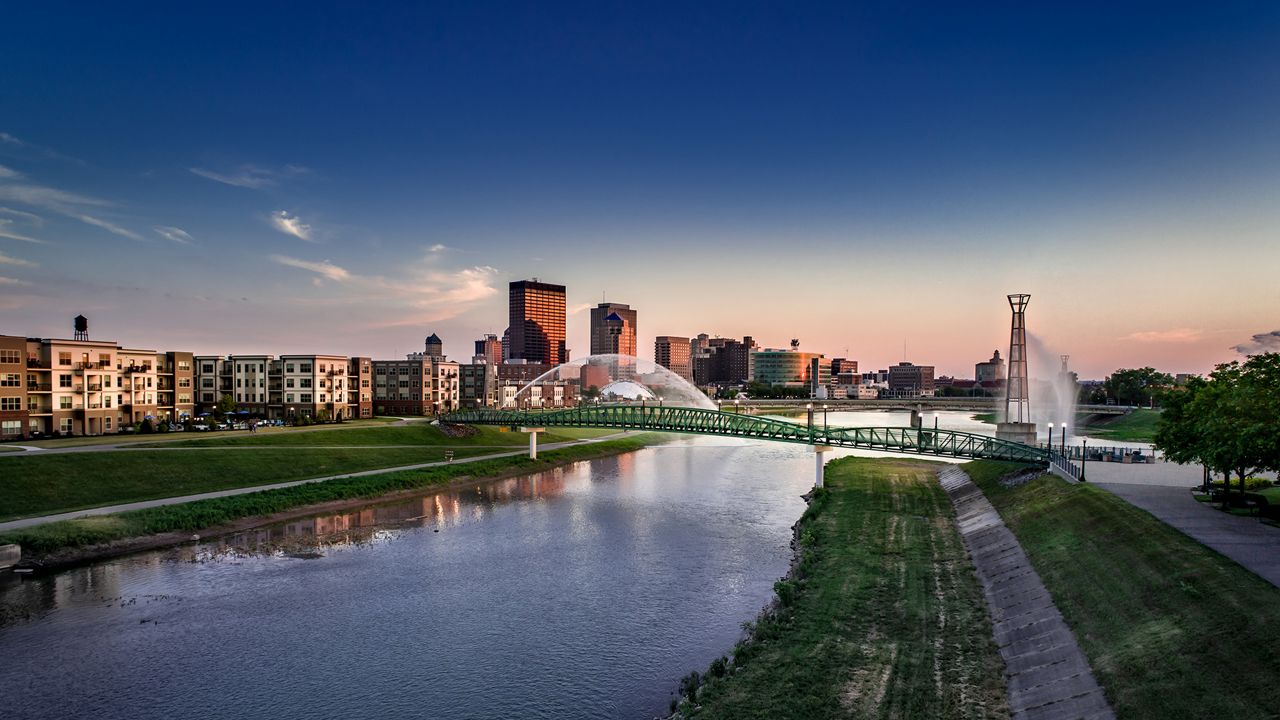 A low aerial view via drone looking up river toward downtown as the sun sets and the river fountains start.