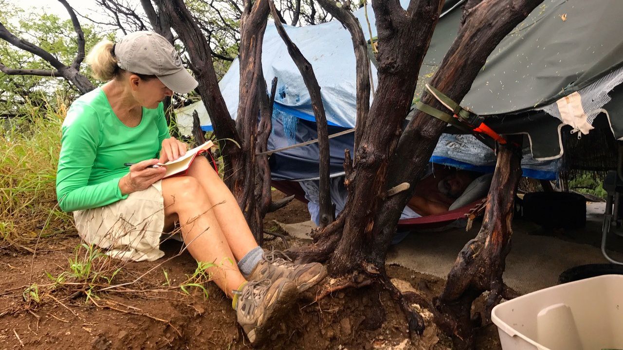 Denby Fawcett interviewing a homeless man, Joseph Kerr, in his tent on the slopes of Diamond Head in 2016. (Photo by Cory Lum, courtesy of Denby Fawcett)