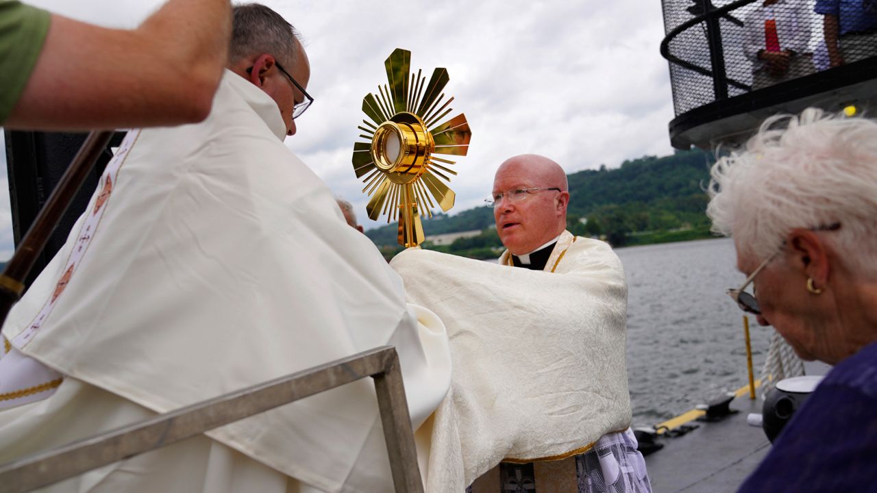 Bishop Edward Lohse, apostolic administrator of the Catholic Diocese of Steubenville, left, hands the Eucharist to the Rev. Roger Landry as they board a boat on the Ohio River as part of the National Eucharistic Pilgrimage, at the Steubenville Marina in Steubenville, Ohio, Sunday, June 23, 2024.