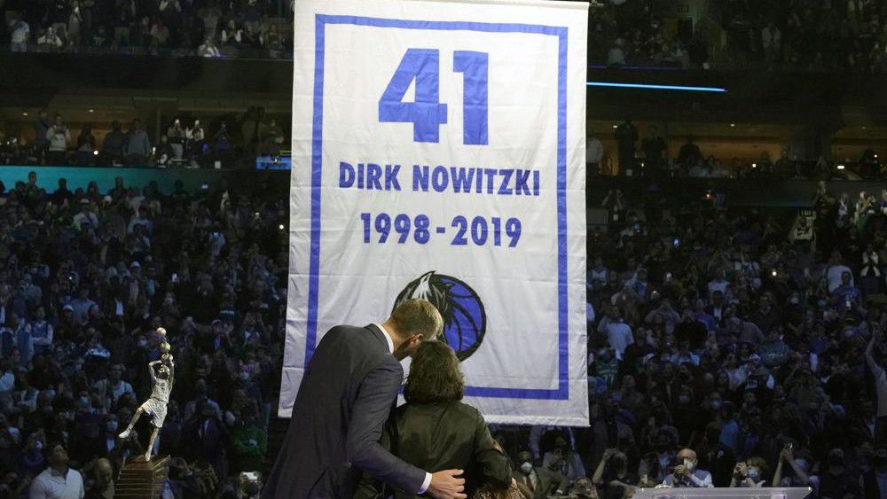 Former Dallas Mavericks Dirk Nowitzki, left, and his wife Jessica Olsson watch a banner being raised during a number retirement ceremony for Nowitzki after an NBA basketball game between the Golden State Warriors and Dallas Mavericks in Dallas, Wednesday, Jan. 5, 2022. (AP Photo/LM Otero)