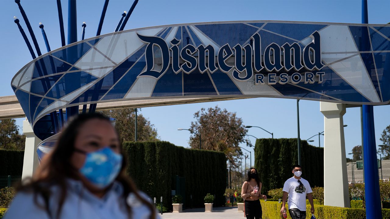 FILE - IIn this March 9, 2021, file photo, a woman with a face mask waits to cross the street outside Disneyland Resort in Anaheim, Calif.  (AP Photo/Jae C. Hong, File)