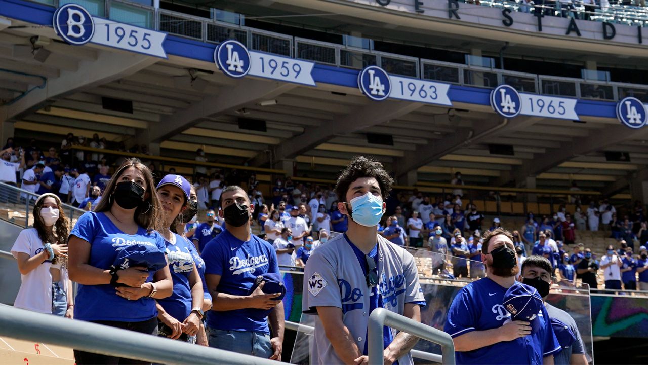 Fans wear masks as the national anthem plays before a baseball game between the Los Angeles Dodgers and the Washington Nationals, Friday, April 9, 2021, in Los Angeles. (AP Photo/Marcio Jose Sanchez)
