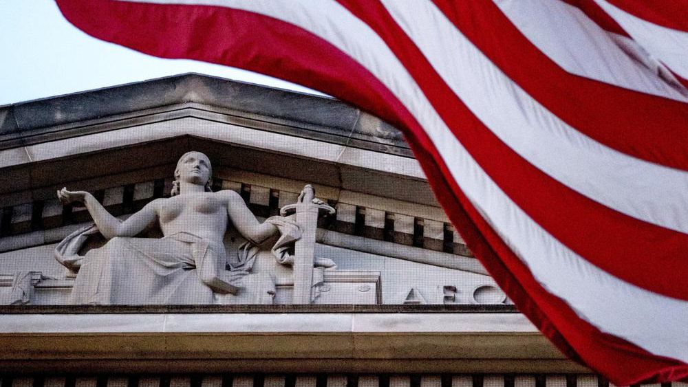 FILE - An American flag flies outside the Department of Justice in Washington, March 22, 2019. (AP Photo/Andrew Harnik, File)