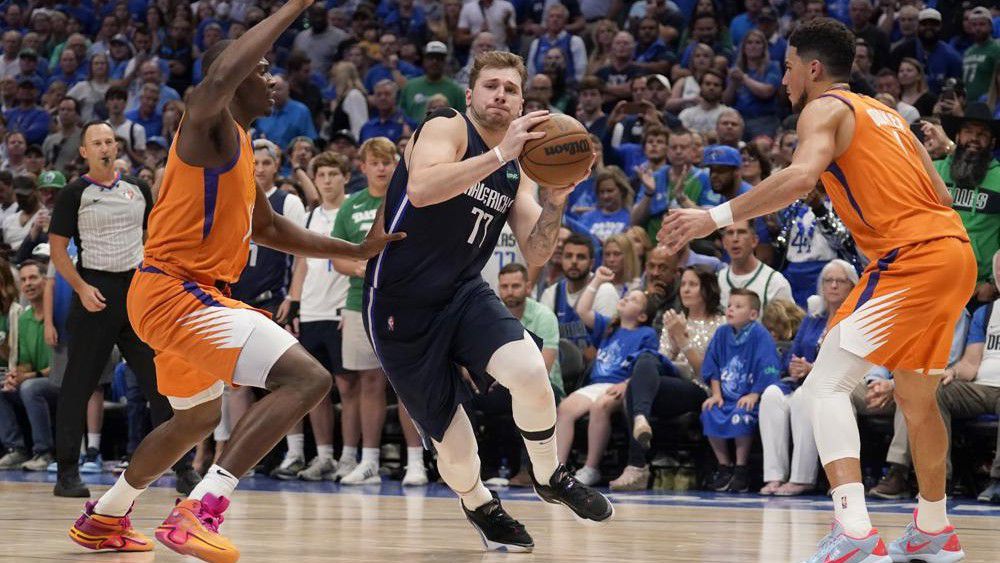 Phoenix Suns center Bismack Biyombo, left, and Devin Booker (1) defend as Dallas Mavericks guard Luka Doncic (77) drives to the basket in the second half of Game 4 of an NBA basketball second-round playoff series, Sunday, May 8, 2022, in Dallas. (AP Photo/Tony Gutierrez)