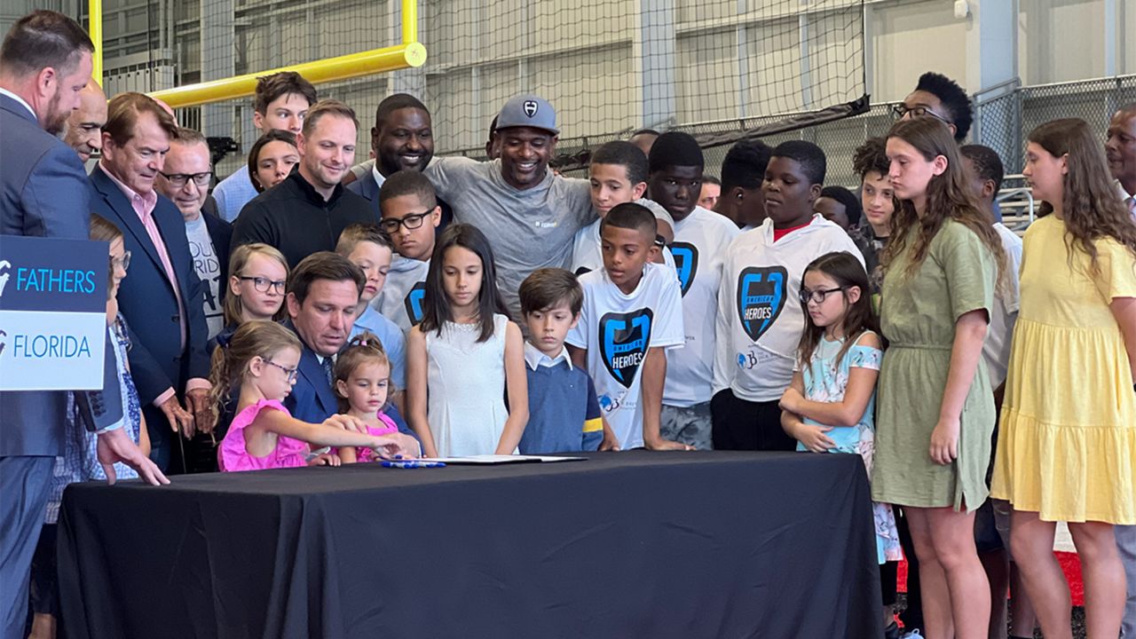 Gov. Ron DeSantis is flanked by former NFL players, coaches and current lawmakers, as well as his daughter Madison as he signs HB 7065 on Monday.