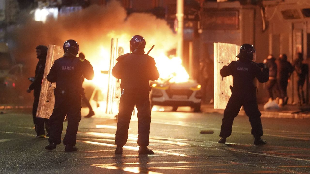 A car burns as Irish policemen stand at the scene of an attack in Dublin city centre, Thursday Nov. 23, 2023. (Brian Lawless/PA via AP)