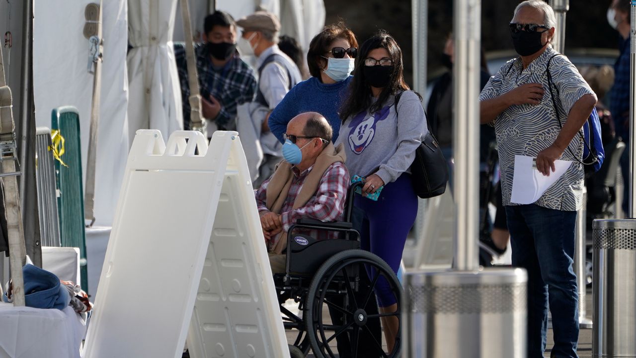 Orange County residents wait in line outside tents for a COVID-19 vaccine at the Toy Story parking lot at the Disneyland Resort Wednesday, Jan. 13, 2021, in Anaheim, Calif. (AP Photo/Damian Dovarganes)
