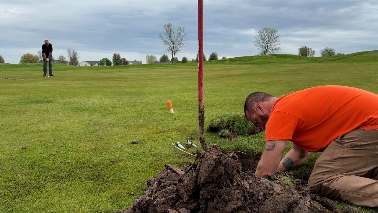Matthew White works on the course with a golfer in the background