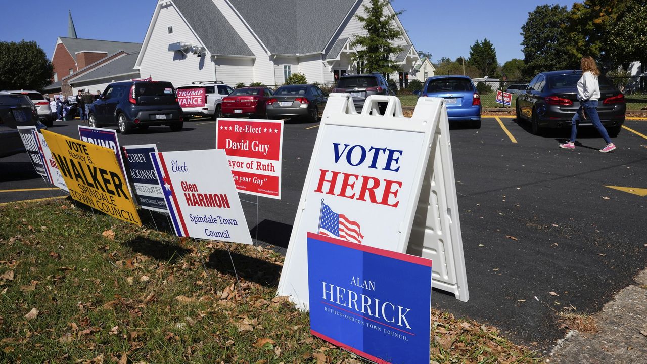 A Vote Here sign is posted amongst political signs as people arrive to vote at the Rutherford County Annex Building, an early voting site western North Carolina. (AP Photo/Kathy Kmonicek)