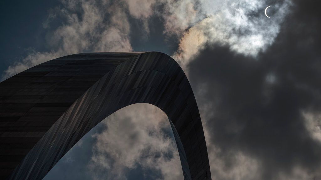 The moon begins to block the sun as a solar eclipse is seen through the clouds over the Gateway Arch, Monday, Aug. 21, 2017, in St. Louis. The Gateway Arch was just a few miles outside of the path of totality. (AP Photo/Jeff Roberson)