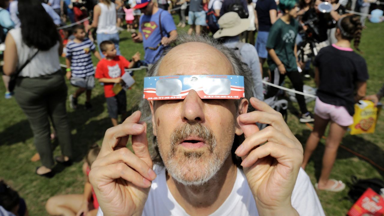 Robert Arthur, of Watertown, Mass., uses protective eclipse glasses to view a partial solar eclipse, Monday, Aug. 21, 2017, on the campus of Massachusetts Institute of Technology, in Cambridge, Mass. (AP Photo/Steven Senne)