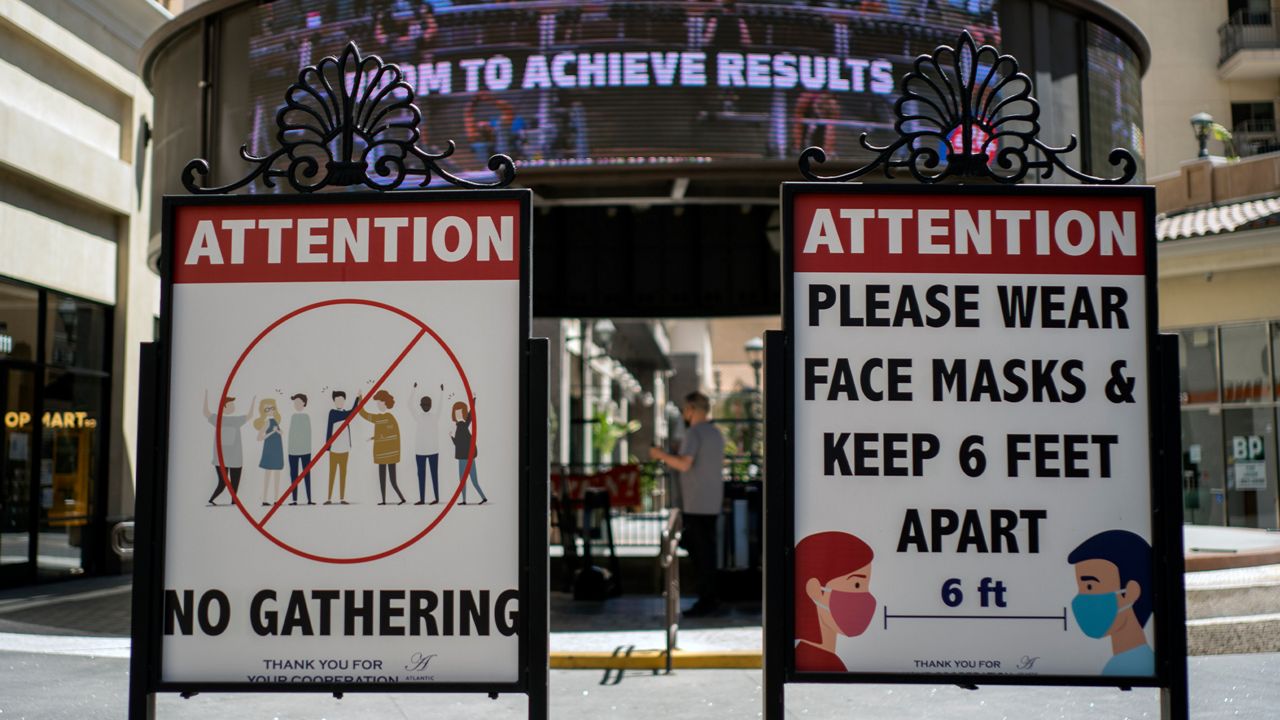 In this June 11, 2021, file photo, signs with social distancing guidelines and face mask requirements are posted at an outdoor mall amid the COVID-19 pandemic in Los Angeles. (AP Photo/Damian Dovarganes, File)