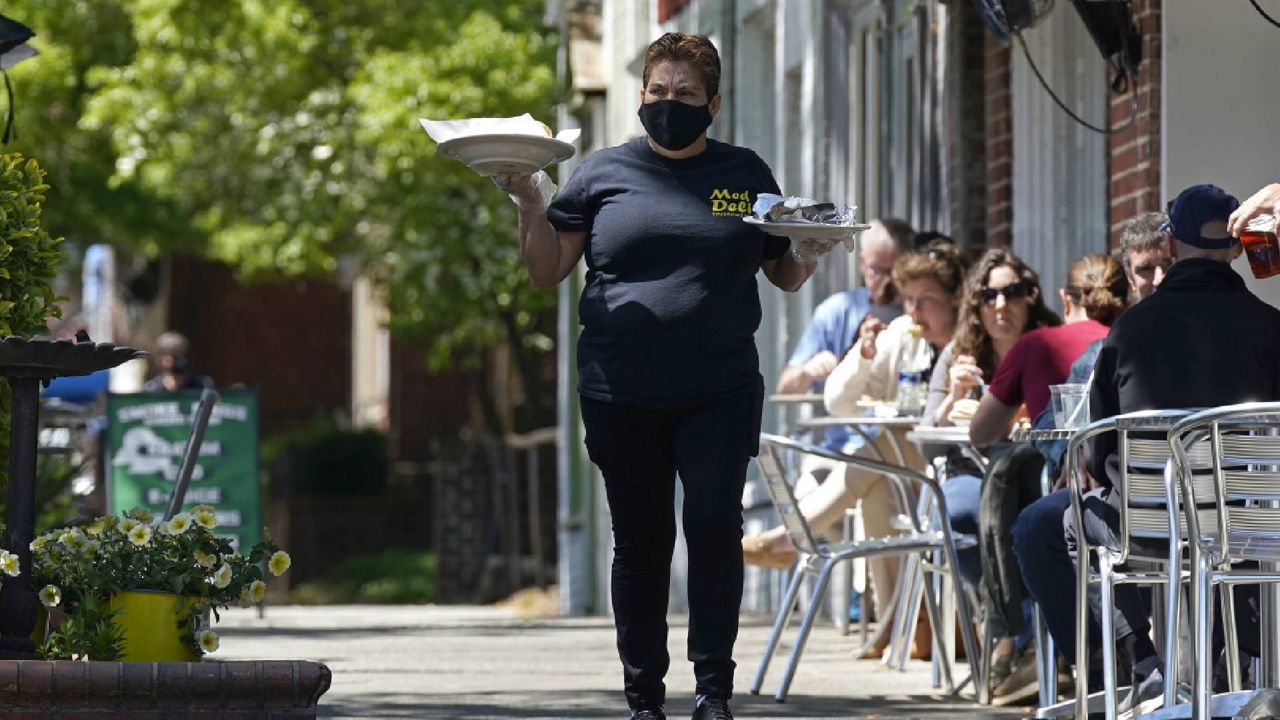 A member of the wait staff delivers food to outdoor diners along the sidewalk at the Mediterranean Deli restaurant in Chapel Hill, N.C., Friday, April 16, 2021. The U.S. economy grew at a brisk 6.4% annual rate last quarter — a show of strength fueled by government aid and declining viral cases that could drive further gains as the nation rebounds with unusual speed from the pandemic recession. (AP Photo/Gerry Broome)