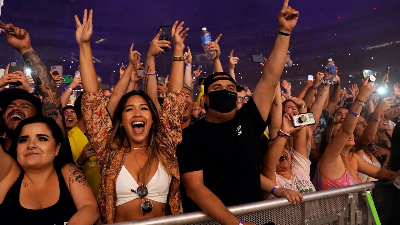 A masked fan is surrounded by unmasked fans during Kaskade's performance at SoFi Stadium, Saturday, July 17, 2021, in Los Angeles. (AP Photo/Chris Pizzello)