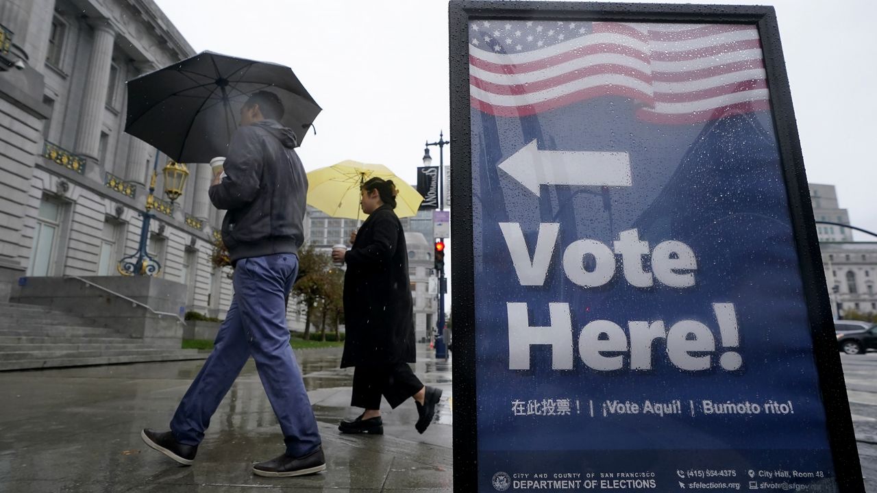 People carry umbrellas while walking past a voting sign outside City Hall in San Francisco, Tuesday, Nov. 8, 2022. (AP Photo/Jeff Chiu)