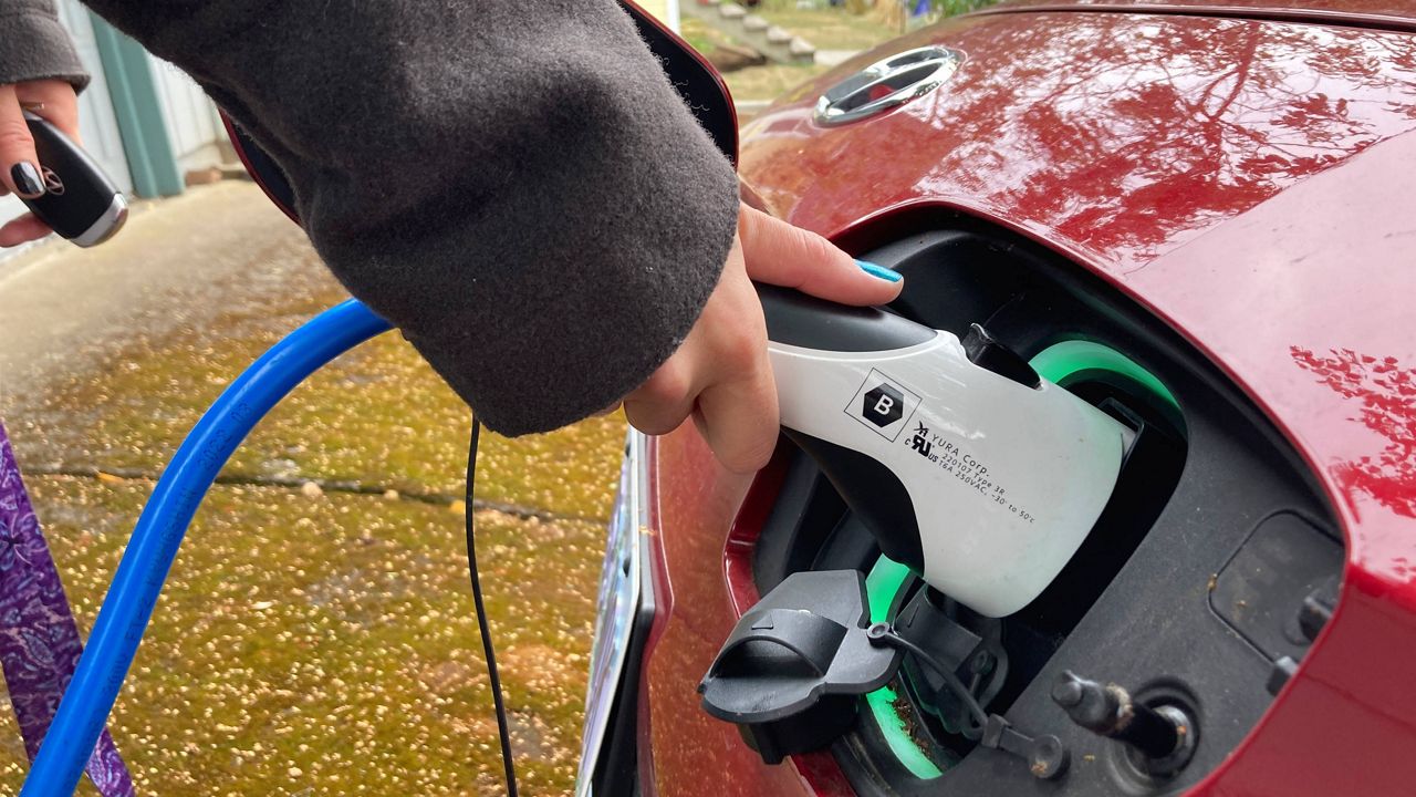 A woman charges her electric vehicle in Portland, Ore. (AP Photo/Gillian Flaccus, File)