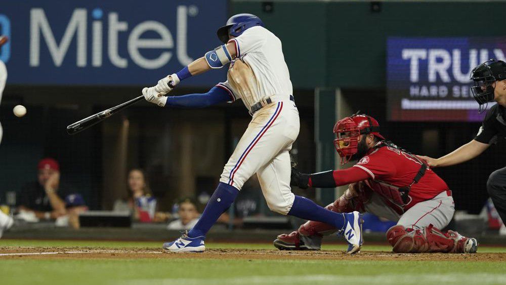 Texas Rangers Eli White, left, hits a two run RBI single in front of Los Angeles Angels catcher Austin Romine (19) during the first inning of a baseball game in Arlington, Texas, Monday, May 16, 2022. Rangers Jonah Heim and Sam Huff scored on the play. The Ranges won 7-4. (AP Photo/LM Otero)