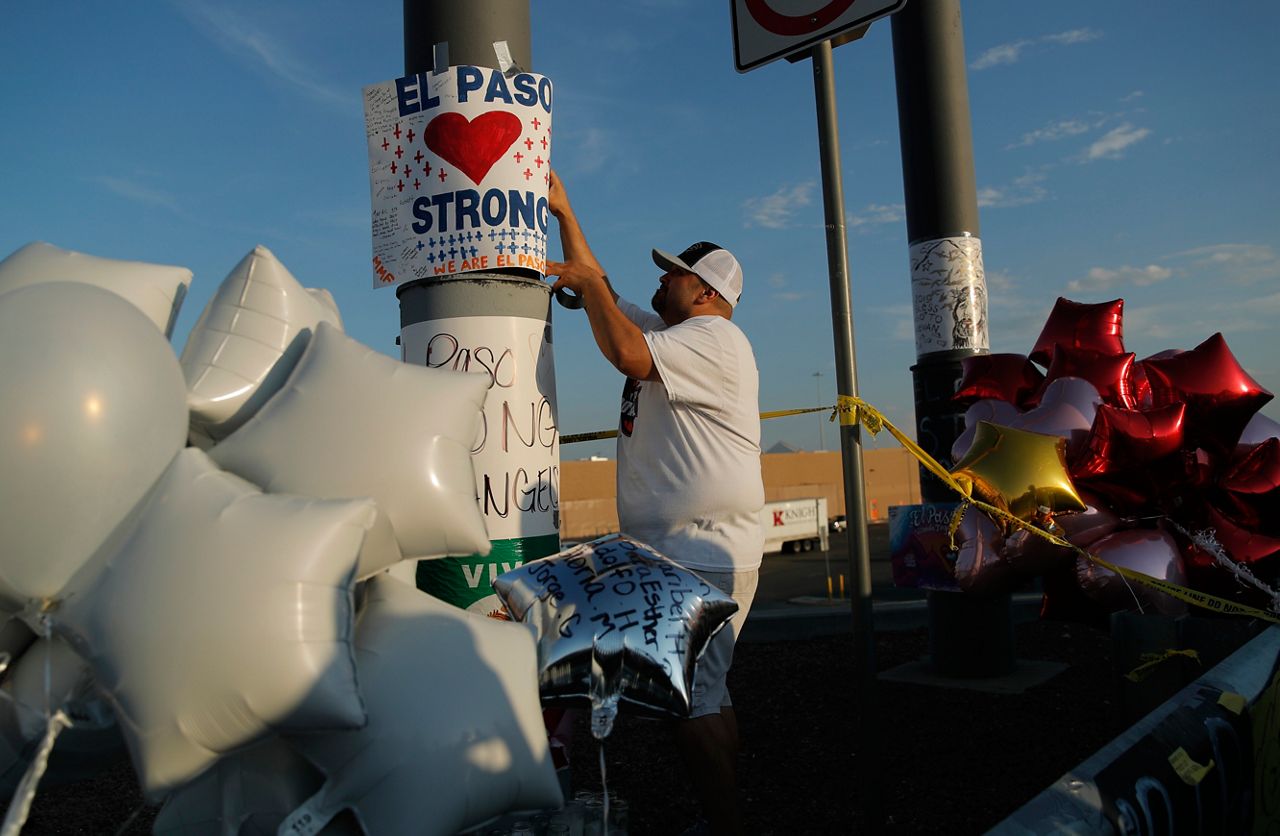 A man hangs up an "El Paso Strong" sign at a makeshift memorial at the scene of a mass shooting at a shopping complex, Tuesday, Aug. 6, 2019, in El Paso, Texas. (AP Photo/John Locher)
