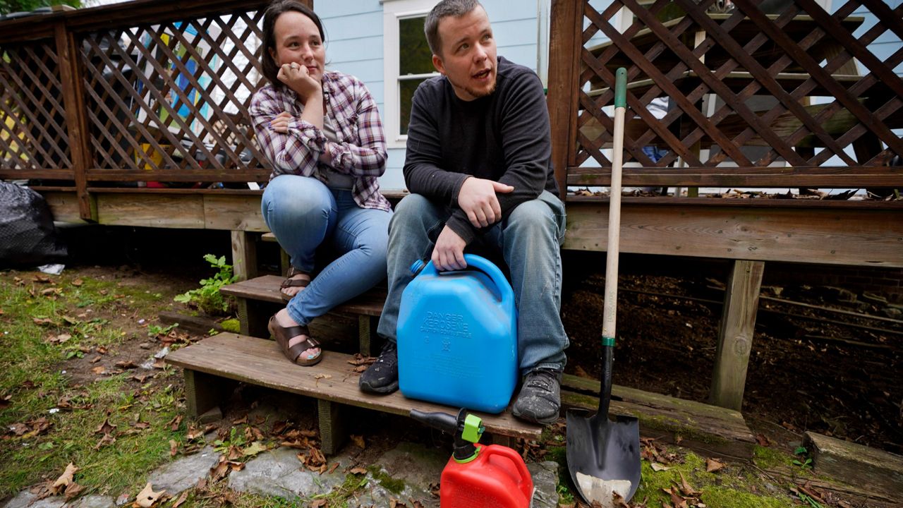 Lucinda Tyler and Aaron Raymo sit outside their home in Jay, Maine, with fuel containers they used to fill their heating oil tank. (AP Photo/Robert F. Bukaty)