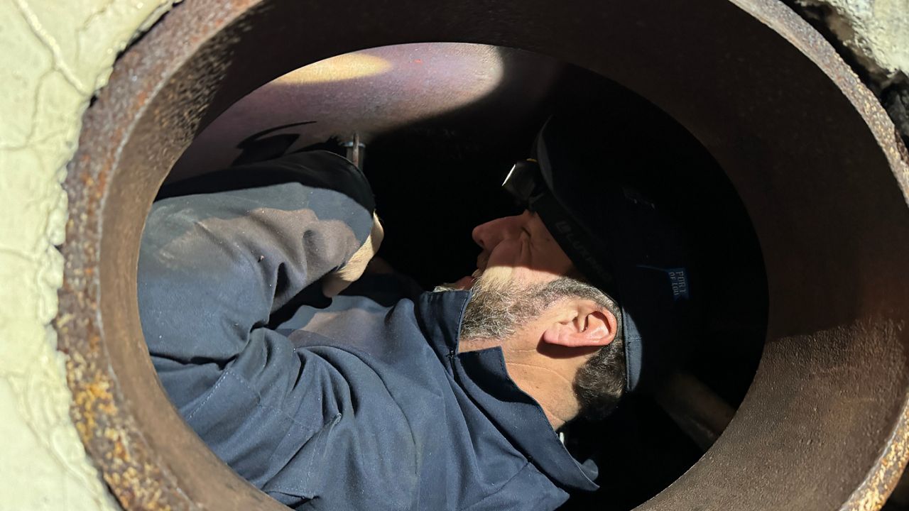 Belle of Louisville Chief Engineer Daniel Lewis squeezes into an opening in the top of the boat’s boiler to remove one of its antique water pressure gauges (Spectrum News 1/Mason Brighton)