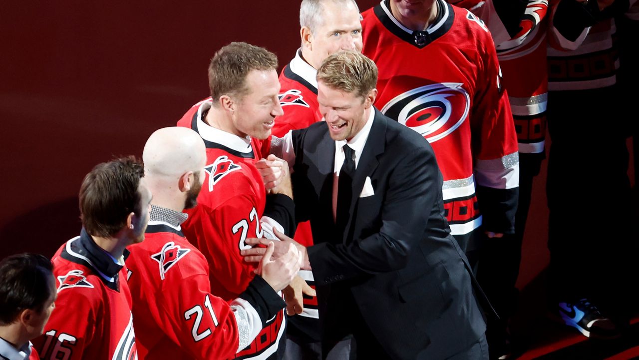 Former Carolina Hurricanes player Eric Staal, right, shakes hands with former teammate Michael Commodore, fourth from left, during a ceremony to retire Staal's No. 12 jersey in Raleigh, N.C., on Sunday, Jan. 12, 2025. (AP Photo/Karl DeBlaker)