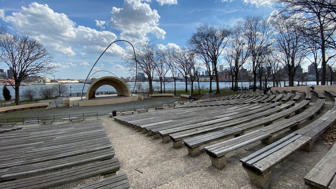 An image of the now-demolished amphitheater in East River Park, showing rows of wood benches in front of the concrete amphitheater, looking towards the East River. 